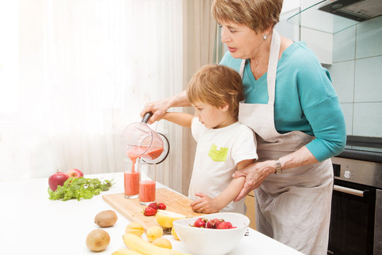 Happy grandmother and her little grandson making smoothie with fresh fruit and berries in the blender in kitchen. Little  boy preparing fruit cocktail or smoothie for breakfast. Healthy eating.