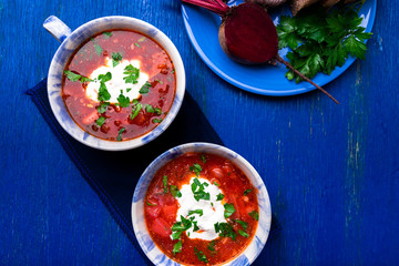 Ukrainian traditional borsch. Russian vegetarian red soup  in blue bowl on blue wooden background.  Borscht, borshch with beet. Two plates. Top view.