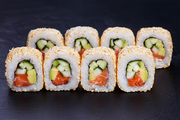 Appetizing fresh california sushi roll with humpback salmon in sesame served on black slate, close up. Japanese healthy seafood