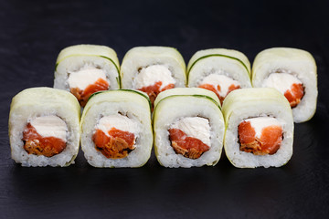 Appetizing fresh sushi rolls in cucumber served on black slate, close up. Tasty Japanese food