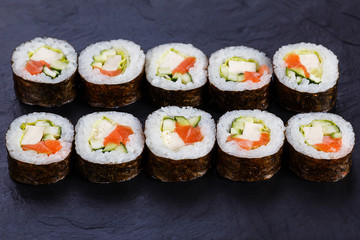 Appetizing fresh maki sushi roll with salmon and tofu cheese served on black slate, close up. Japanese healthy seafood.