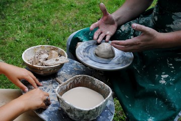 Potter's hands guiding child's hands to help him to work with the pottery wheel