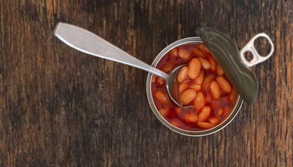 Canned beans in a tin with spoon on wooden background