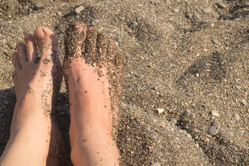 Vacation concept. Sandy woman feet on the beach and brown sand with little rocks