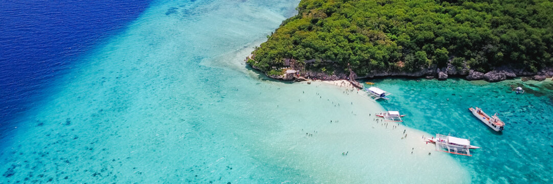 Fototapeta Aerial view of sandy beach with tourists swimming in beautiful clear sea water of the Sumilon island beach landing near Oslob, Cebu, Philippines. - Boost up color Processing. Panoramic banner.