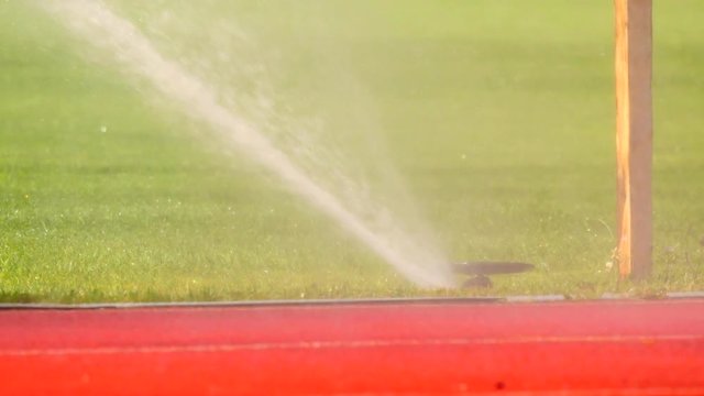Soccer or football field irrigation system of automatic watering grass. Watering the football playing field, red rubber racetracks in outdoor stadium