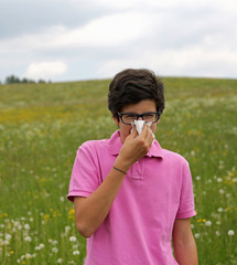 Allergic boy with glasses blows his nose using a white handkerch