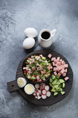 Black wooden serving board with okroshka or cold soup with kvass, vertical shot on a grey stone background, high angle view
