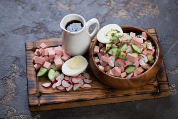 Bowl with traditional russian cold soup okroshka on a wooden serving board, horizontal shot on a brown stone surface
