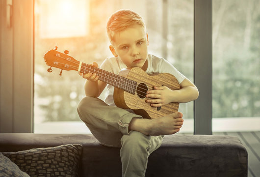 Young boy play on guitar at home at sunny day. Boy play on ukule