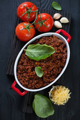 Top view of freshly made bolognese sauce with some of its cooking components on a black wooden background