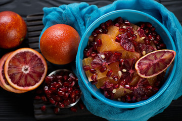 Fruit salad with oranges and pomegranate seeds, high angle view on a black wooden surface, horizontal shot