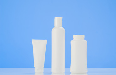 Set of tubes and containers of cream or gel in white plastic packaging. Product mockup with mirror reflection on white table with blue background.