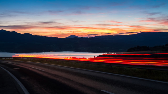 Austrian countryside road car is passing during the sunset only light rays are visible lacke is on the background