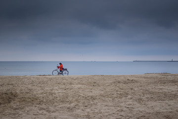 a woman ride a bike by the sea on a cloudy day