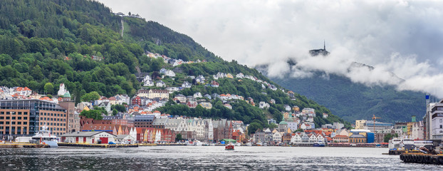 Naklejka premium Panorama of historic, UNESCO World Heritage listed district Bryggen in Bergen. Visible hills Floyen with upper funicular station and Ulriken with characteristic top tower