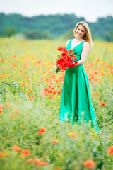 Naklejka na ściany i meble A woman with charming smile during light rain with a bouquet of poppies among the flowering meadow in the summer.