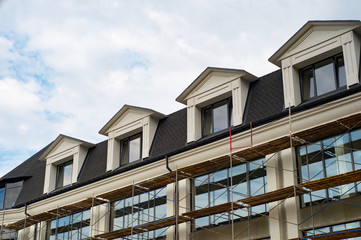 Photo of construction of a new office center with lovely mansard roof and dormers, on blue sky background