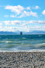 Seascape, ship floating away into the distance, mountains, sky, stones