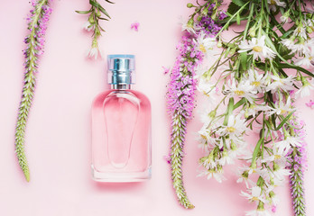 Floral perfume bottle with fresh herbs and flowers on pink background, top view.  Beauty concept