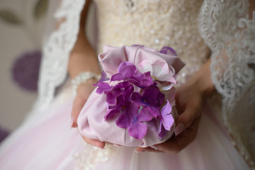 Horizontal shot of bride dressed in lilac wedding dress with embroidered veil, holding delicate wedding mini bucket bag with purple floral details for small necessities.