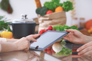 Close-up of four human hands are gesticulate over a tablet in the kitchen. Friends having fun while choosing menu or making online shopping. So much ideas for tasty cooking. 