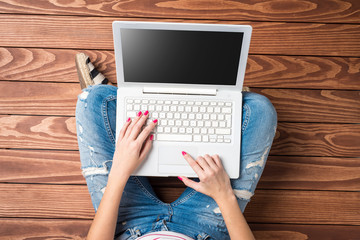 Woman using modern laptop while sitting on wooden floor. Top view