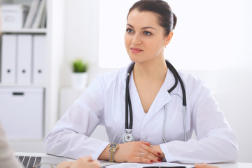 Fototapeta na wymiar Brunette female doctor talking to patient in the hospital office. Physician says about medical exams results for choosing optimal treatment. Healthcare and medicine concept