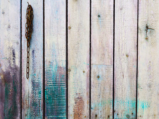 Старый деревянный забор, окрашенный старой краской с прибитым гвоздем и цепью на нем.