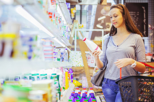 Young Woman Buying Milk In Supermarket. Side View