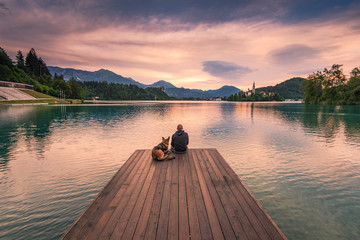 Man and dog sitting on wooden deck at Bled lake, Slovenia - Powered by Adobe