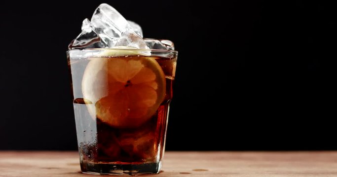 glass with ice cubes and lemon slide and cola. rom cola, fresh drink, ice cubes and bubbles