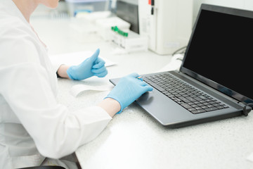 Modern technology in science. Scientist entering data of analysis results to laptop at laboratory