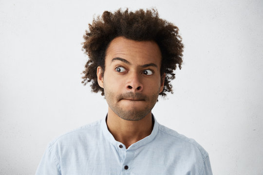 Pleasant-looking guy with African hairstyle having hesitation pressing his lips and looking aside trying to make decision. Dark-skinned male model being worried about something having no ideas