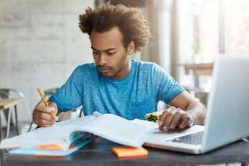 Candid shot of concentrated Afro American hipster male in blue T-shirt preparing for examination...