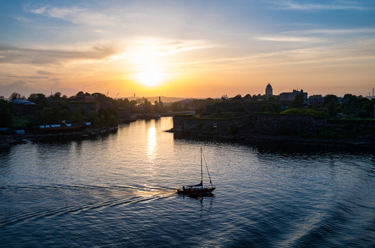 Sailboat is passing near UNESCO heritage fortress Suomenlinna during the sunset reflecting in the water
