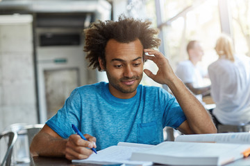 Portrait of handsome African American male with bushy hair sitting at desk in university canteen...