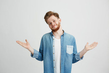 Portrait of young handsome man smiling looking at camera shrugging over white background.