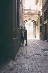 Fototapeta na wymiar A bearded man in a cap wants to kiss his girlfriend while standing beside the building wall on a side street. Beautiful woman is looking with love at her beloved man during romantic dating.