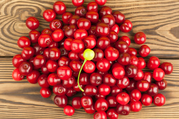 Many red and one green fresh cherries on wooden background