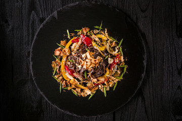 soba noodles of buckwheat Noodles of buckwheat yellow and red pepper, herbs. Pan-Asian cuisine. On stone tray on dark wooden table.