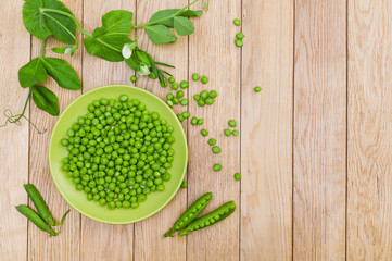 Young green peas on a plate on a wooden background