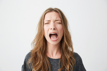 Portrait of emotive young beautiful girl shouting with closed eyes over white background.