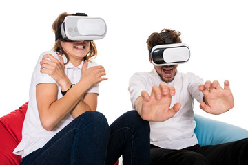 Excited young couple experiencing virtual reality seated on beanbags isolated on white background