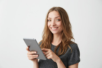 Young pretty girl smiling looking at camera surfing web browsing internet on tablet over white background.