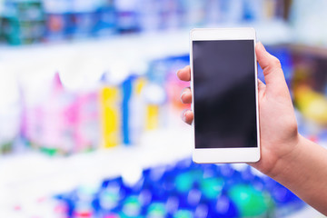 Female hand holding mobile smart phone on supermarket dairy product section in background, business concept.