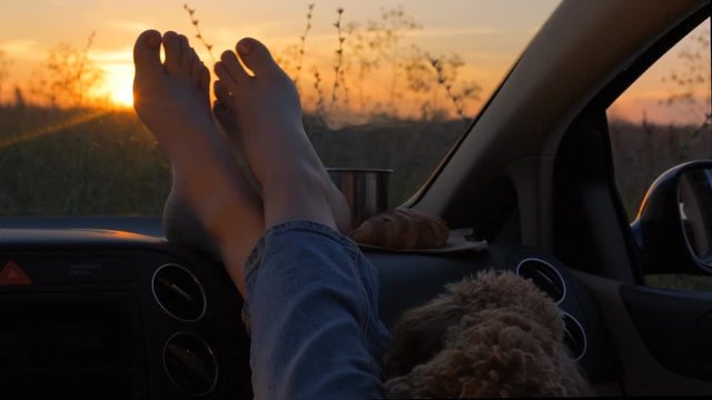 Woman feet on car dashboard. Drinking take away tea and сroissant .