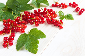 Berries of juicy red currant and leaves on a light wooden background. The pattern with copy space is flat lay