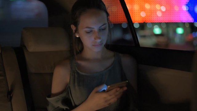 Young adult female in taxi using smart phone.