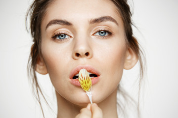 Close up of beautiful young girl with perfect clean skin and alstroemeria petals looking at camera over white background. Facial treatment. Beauty and spa.